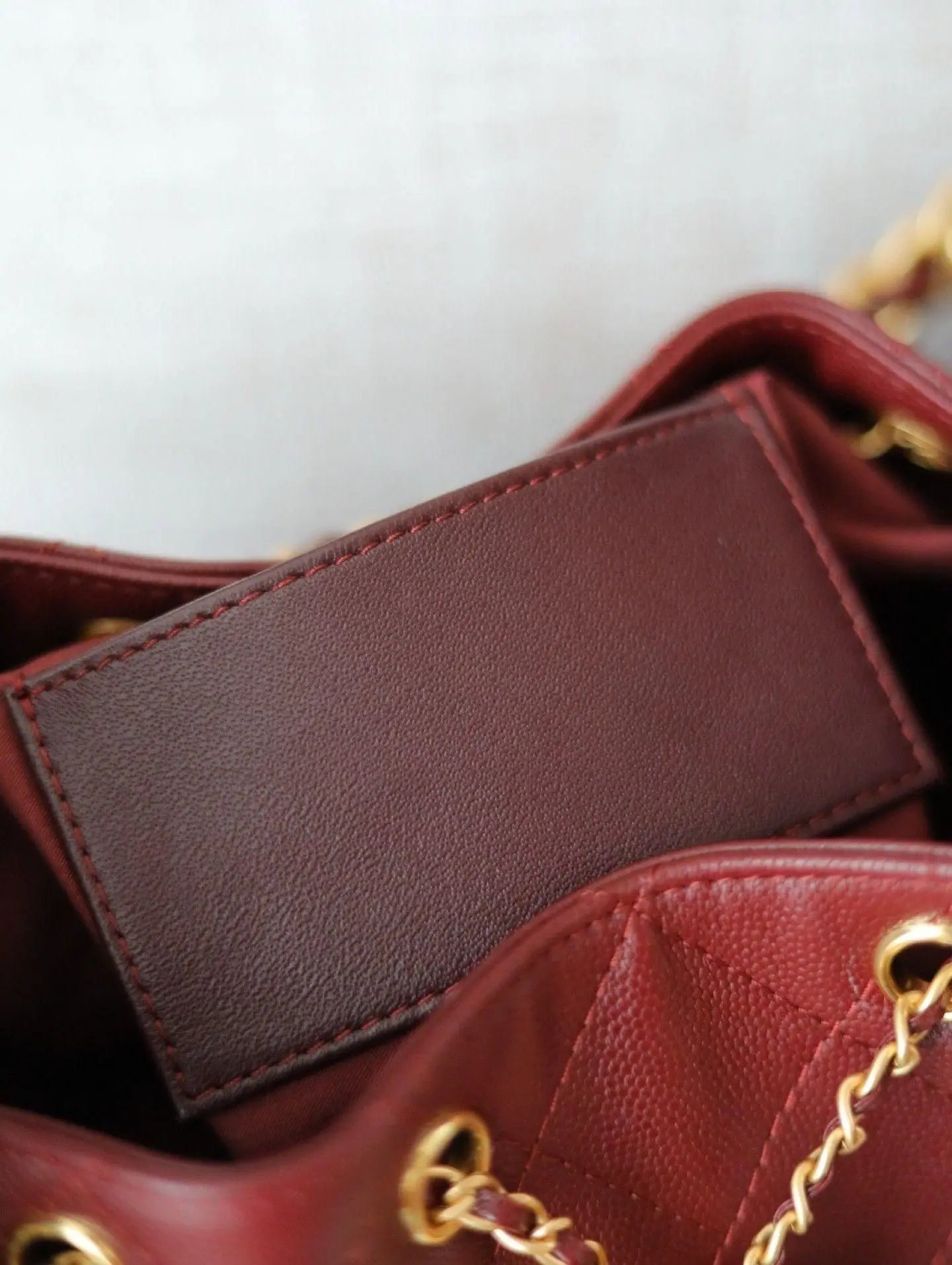 Red rhombus check drawstring bucket bag with a vintage metal chain shoulder strap and layered flap design.
